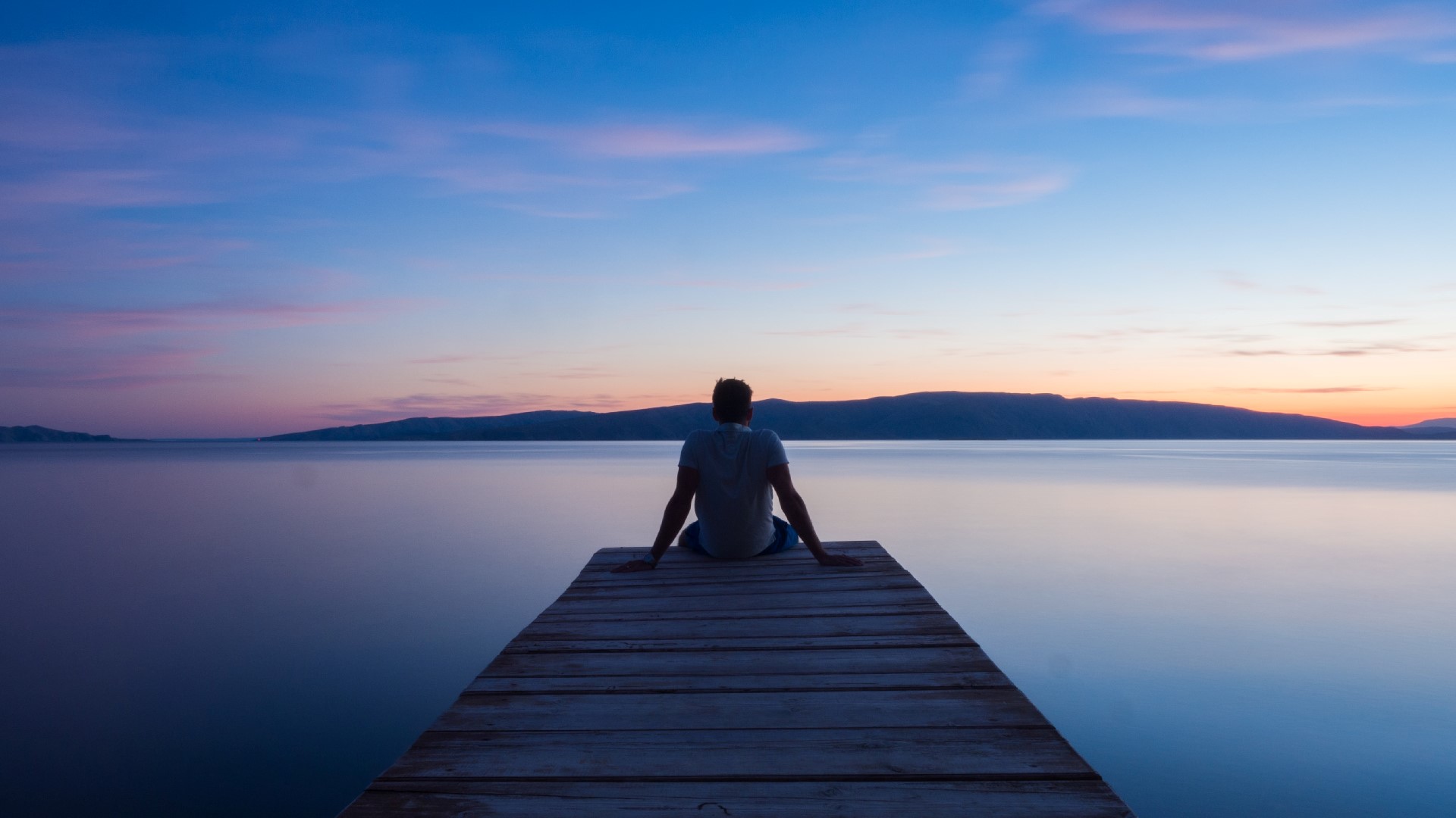 An image of a person sitting on a pier overlooking the ocean