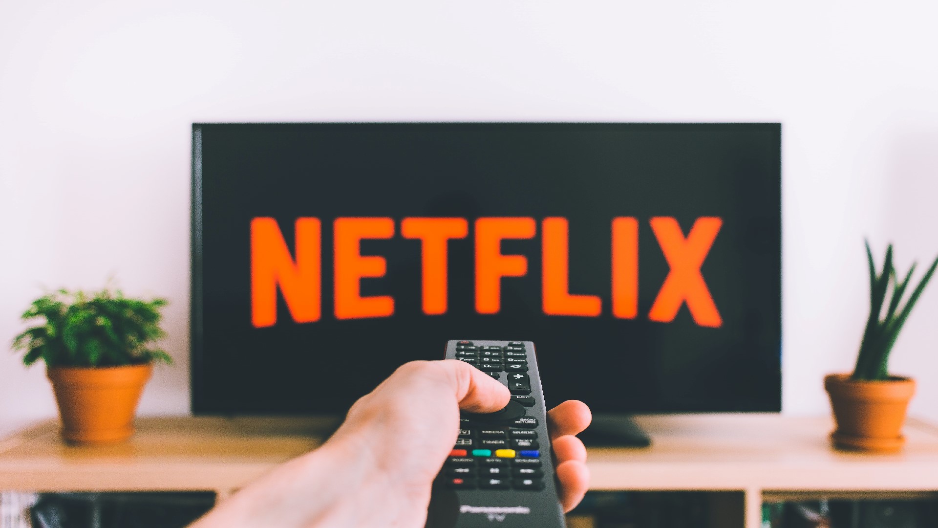 An image of a person holding a remote with Netflix in the background