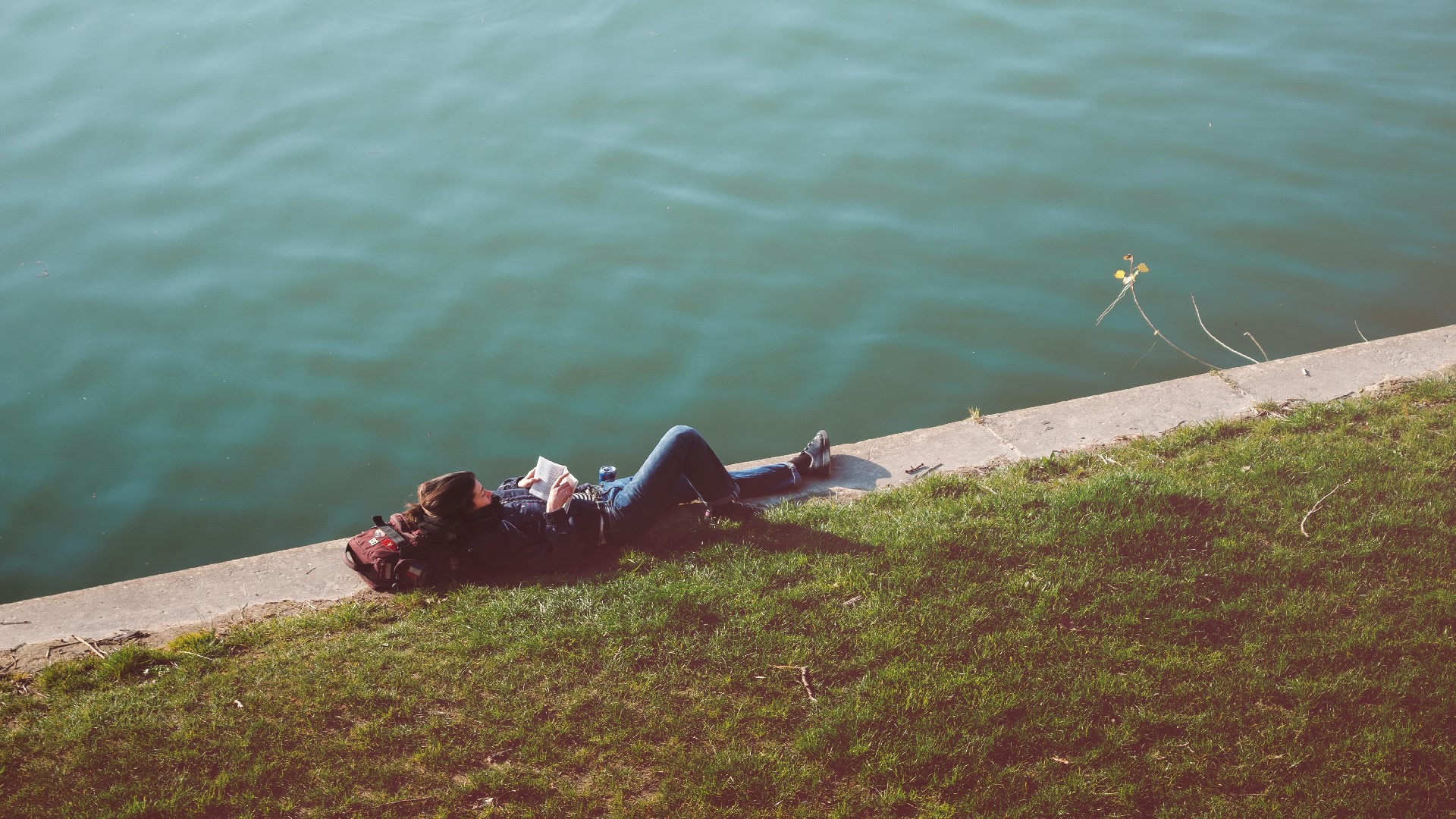 An Image of a girl sitting on a pier reading a book