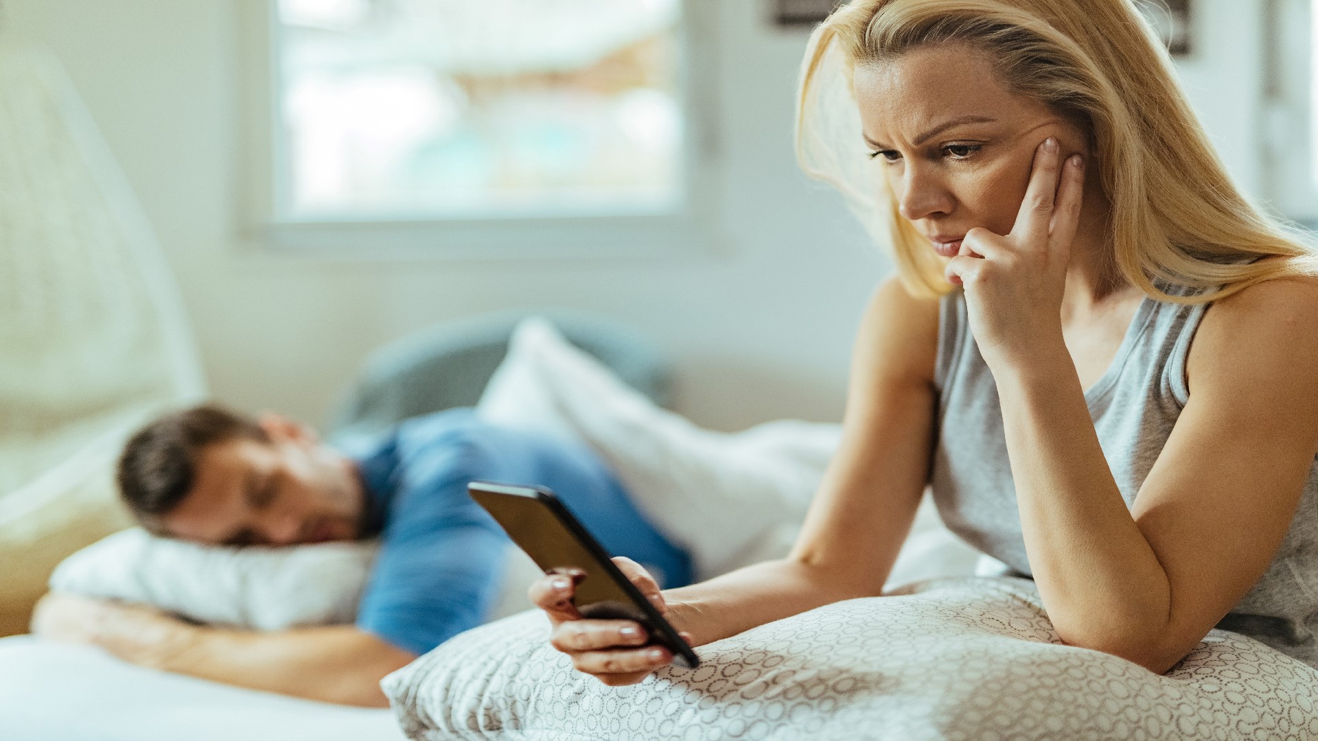 An Image of a Woman with a Phone in her hand while her partner is Sleeping