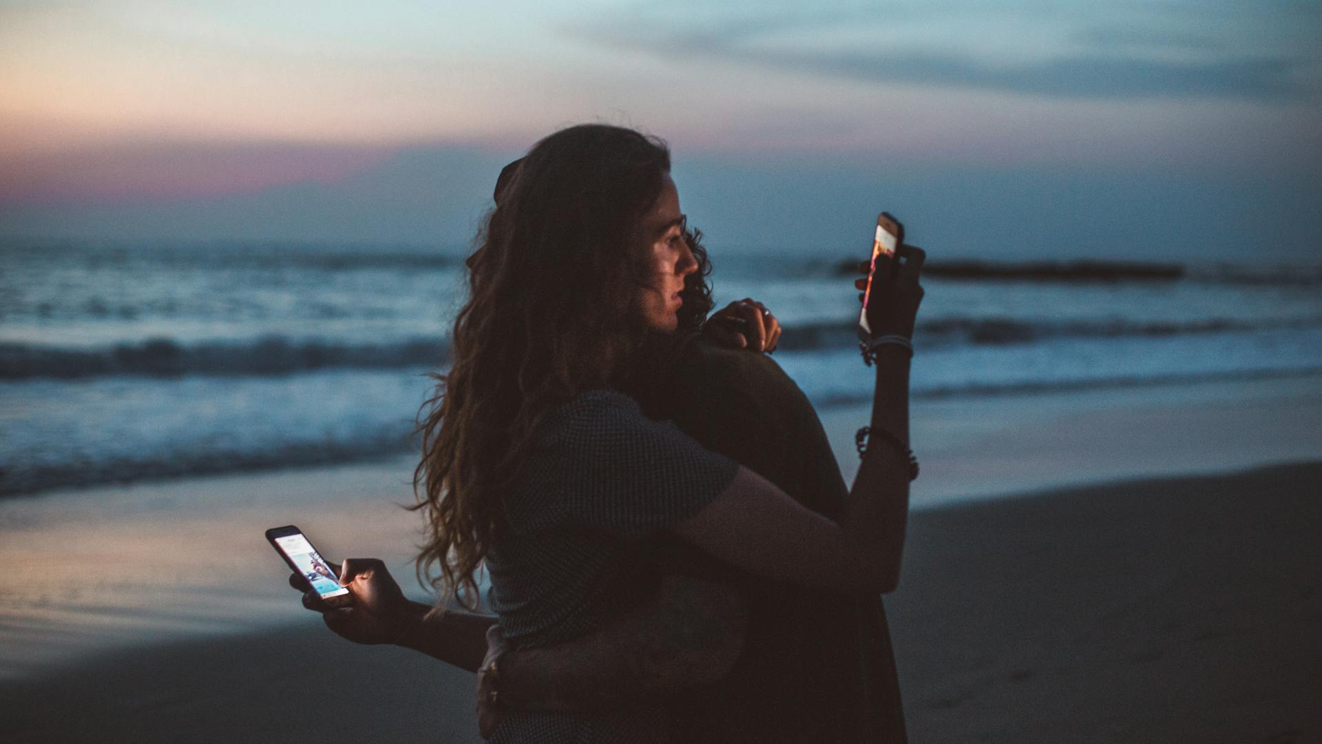 two people hugging each other holding smartphones